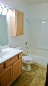 A white toilet sits in a bathroom next to a sink and bathtub.